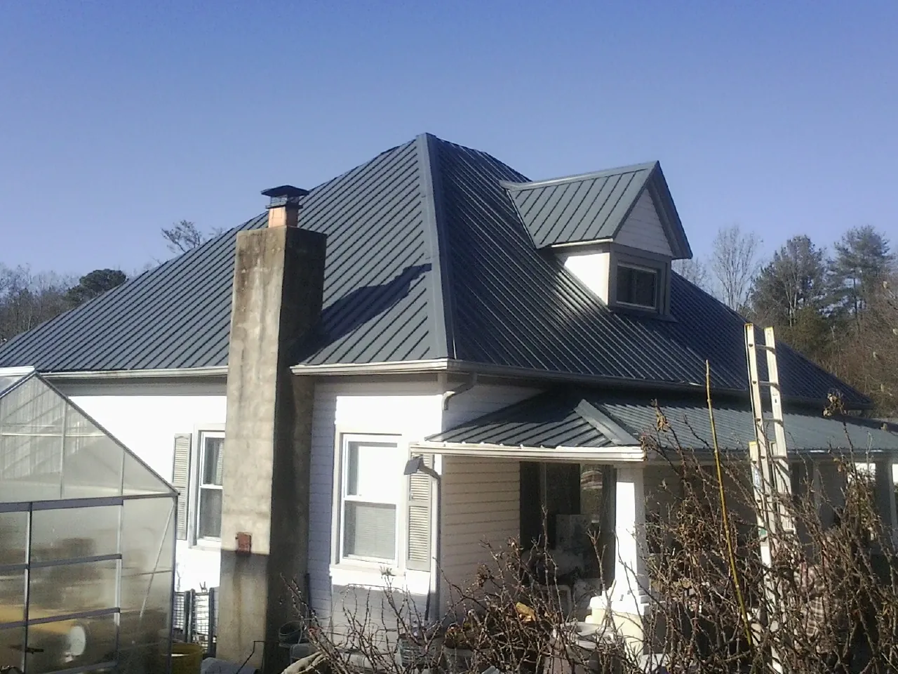 Dark blue standing seam metal roof on a white farmhouse with dormer — Slate & Tile Roof Repair by Roofing Brothers in Hendrix