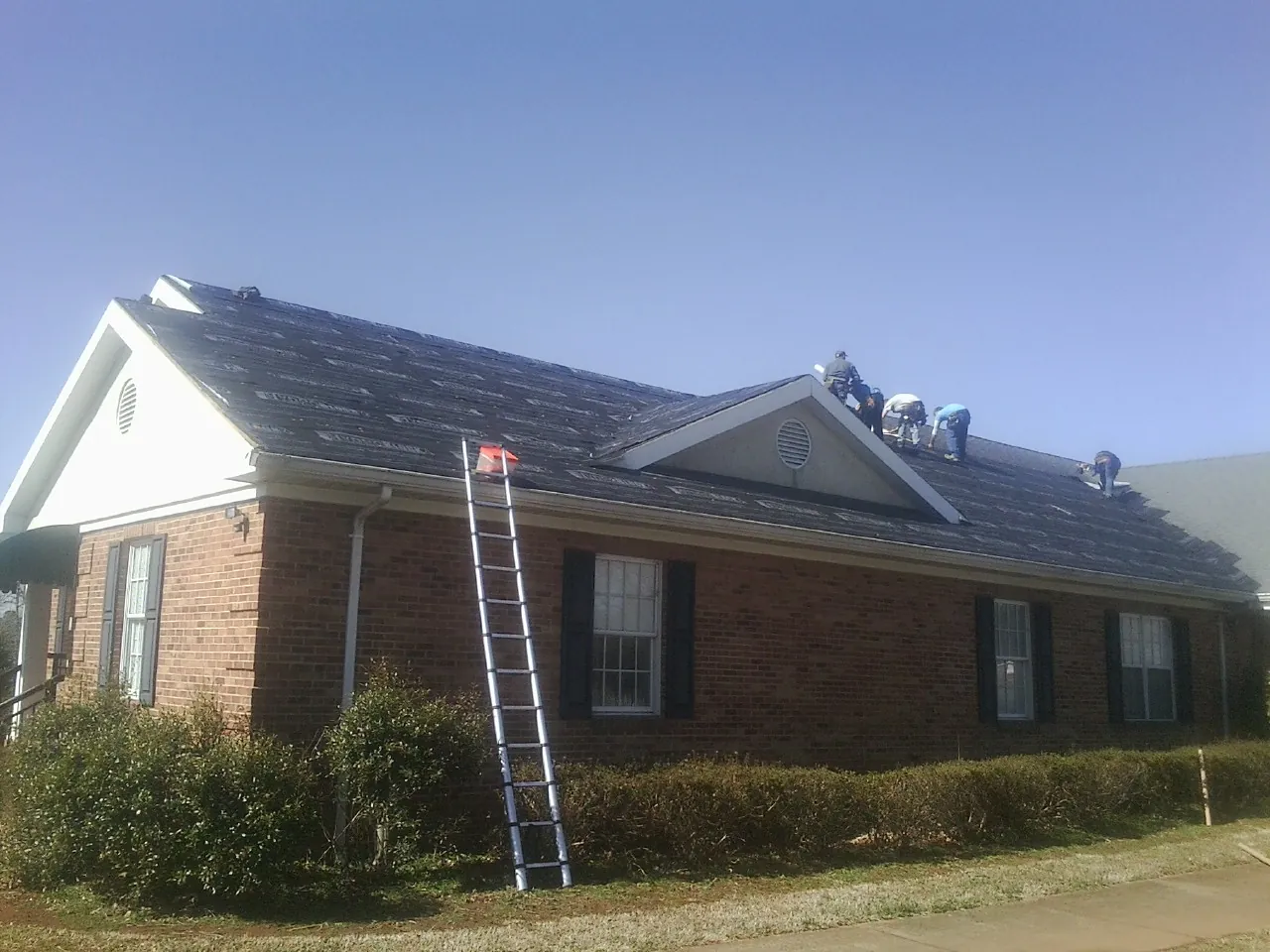 Crew tearing shingles off a brick ranch roof with a ladder set — Metal Roof Repair work by our crew in Hendrix