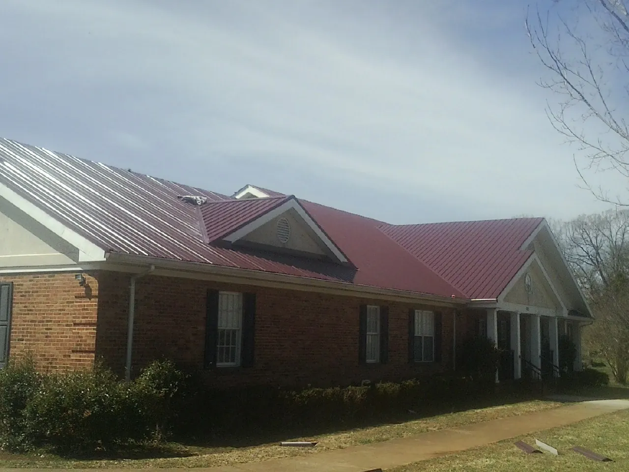 Red metal roof with gabled entries on a long brick building, from a Hail Damage Roof Repair job in Hendrix
