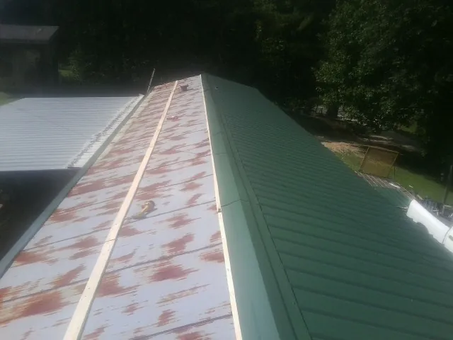 Old rusted panels beside newly installed green metal roofing — Wind Damage Roof Repair by Roofing Brothers in Hendrix