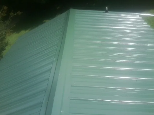 New green metal panels meeting at the ridge of a roof — Flat Roof Repair work by our crew in Hendrix