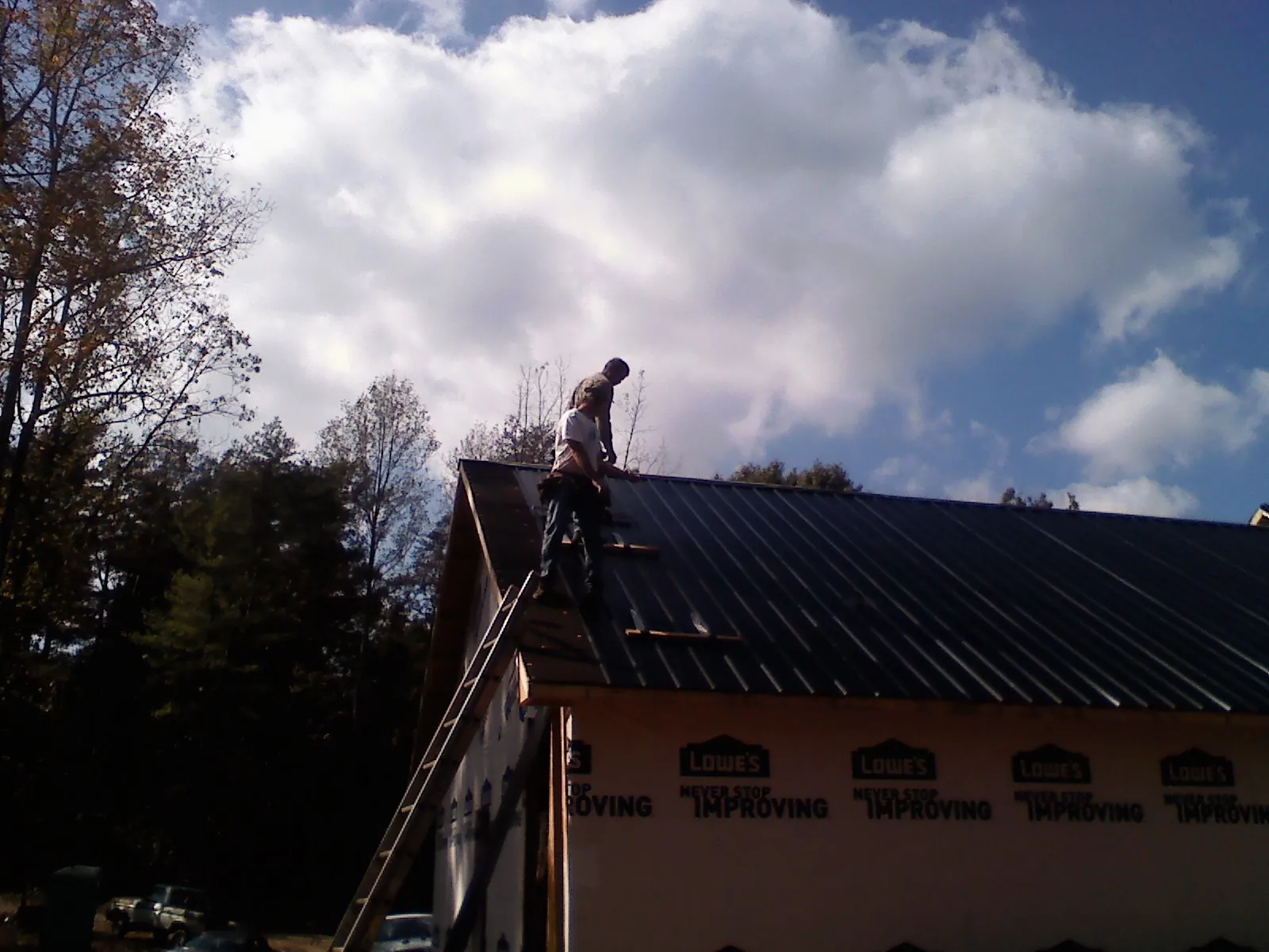 Roofer fastening dark metal panels high against a cloudy sky, from a Roof Inspection job in Hendrix