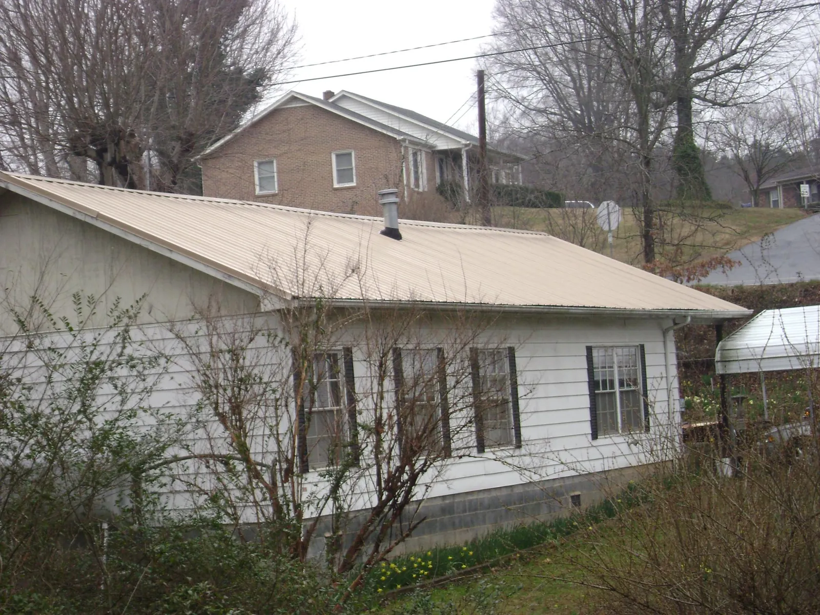 Tan metal roof on a white sided house set into a hillside — Commercial Roofing by Roofing Brothers in Hendrix
