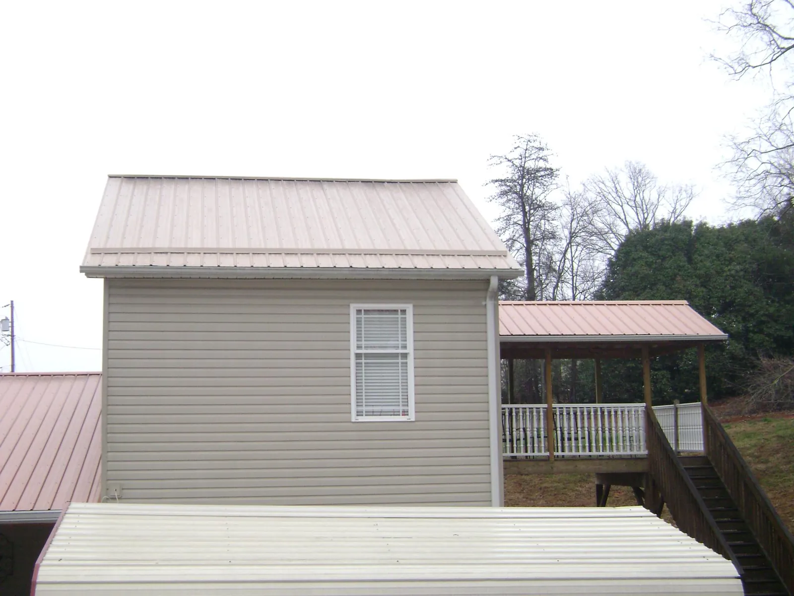 Tan metal roofs on a two story addition and attached porch, from a Roof Replacement job in Hendrix